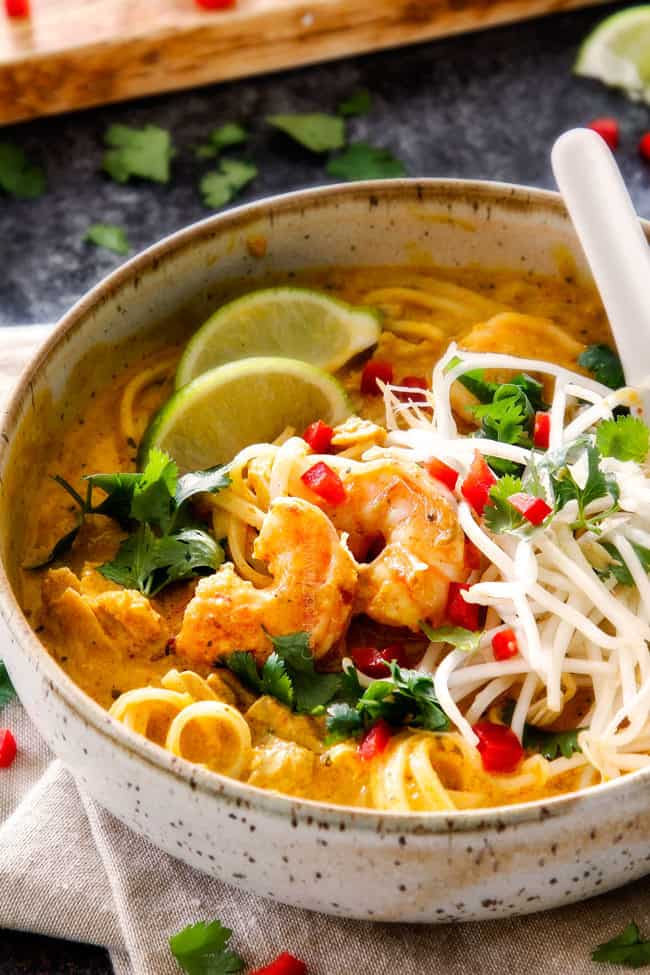 side view of a bowl of laksa soup with bean sprouts, shrimp, chicken and cilantro