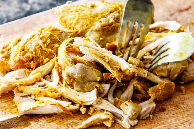 showing how o make laksa by shredding chicken on a wood cutting board