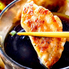 up close of two chopsticks holding a potsticker getting ready to dunk it in potsticker dipping sauce