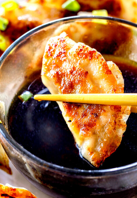 up close of two chopsticks holding a potsticker getting ready to dunk it in potsticker dipping sauce