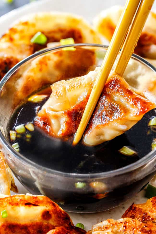 two chopsticks dunking a crispy potsticker in soy vinegar dipping sauce