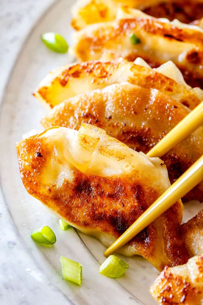 chopsticks picking up a potsttickers from a line of potstickers on a platet