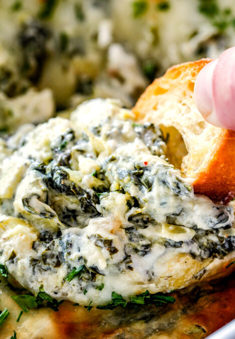 up close of a piece of bread dipping into spinach and artichoke dip