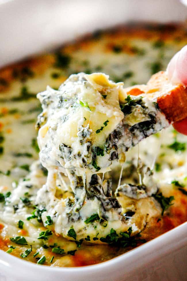 up close of bread being pulled from hot spinach artichoke dip with cheese