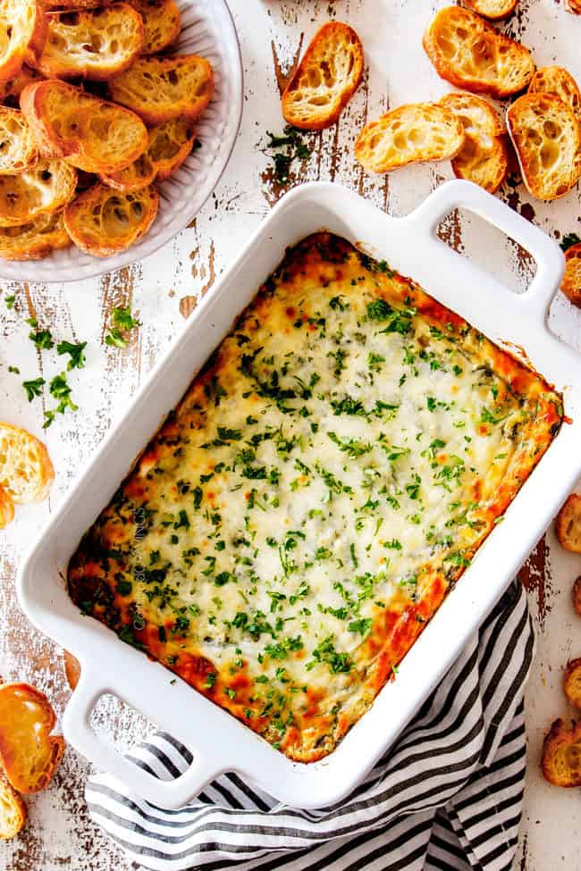 top view of hot spinach artichoke dip baked in a white dish with French bread around for dippers