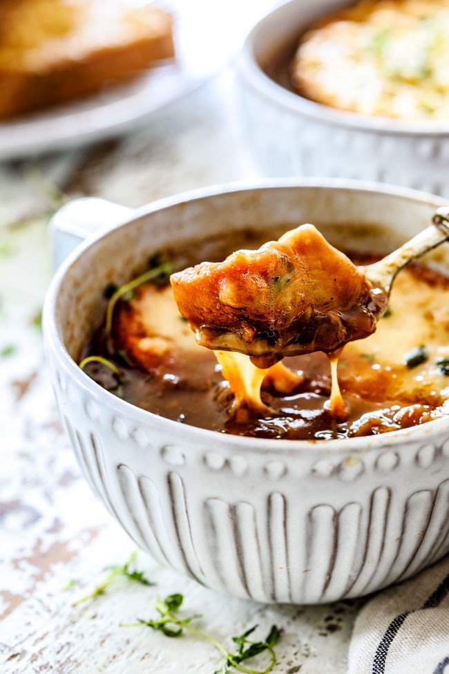 far away of a spoonful of traditional French Onion Soup holding a piece of cheesy baguette