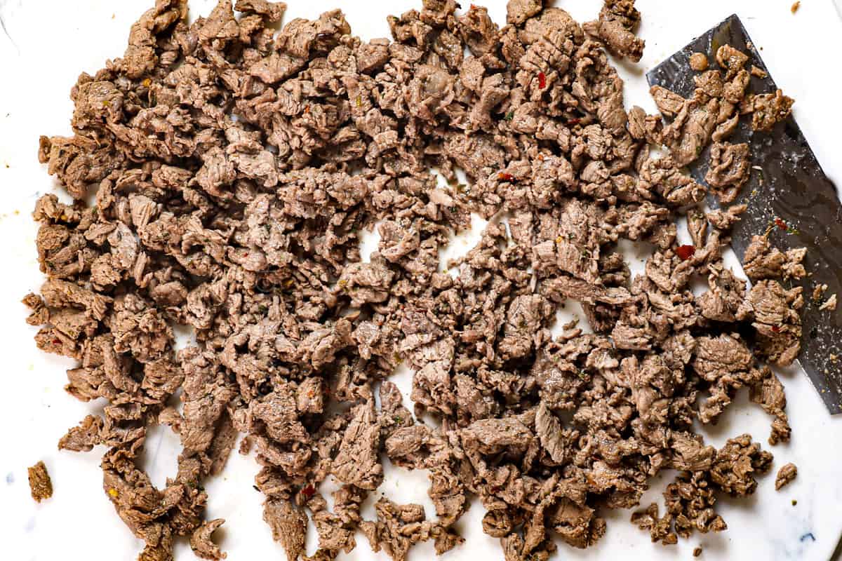 showing how to make Philly cheesesteak by chopping the meat finely on a cutting board