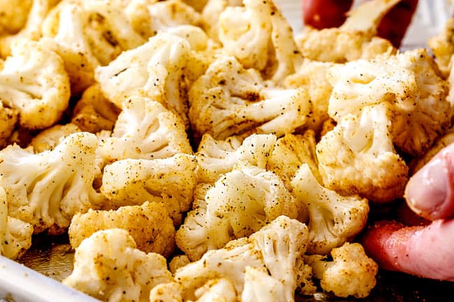 showing how to make roasted cauliflower by tossing with olive oil and seasonings on a baking sheet