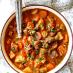 two hands holding a bowl of old fashioned beef stew showing what's in it: beef, potatoes, carrots, celery, onions, garlic, gravy