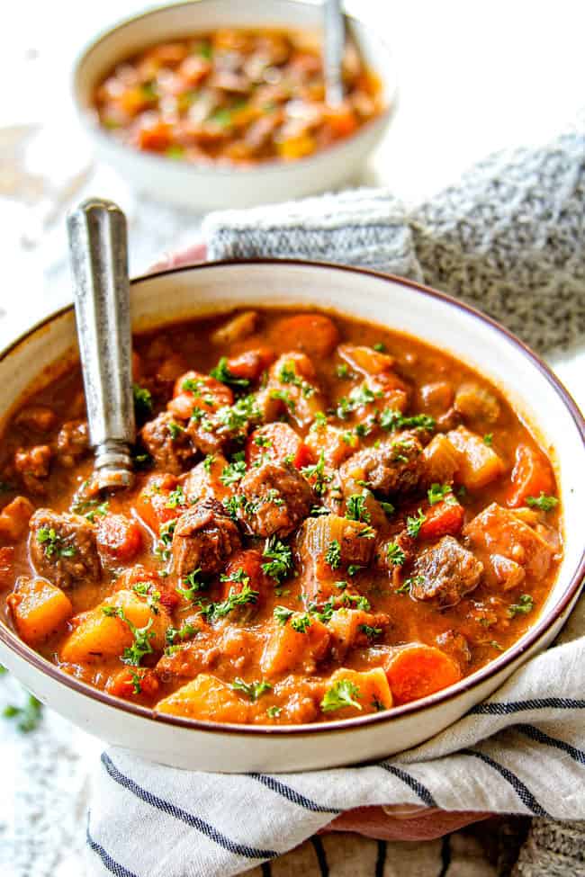 two hands showing how to serve beef stew by holding with two hands and garnishing with parsley