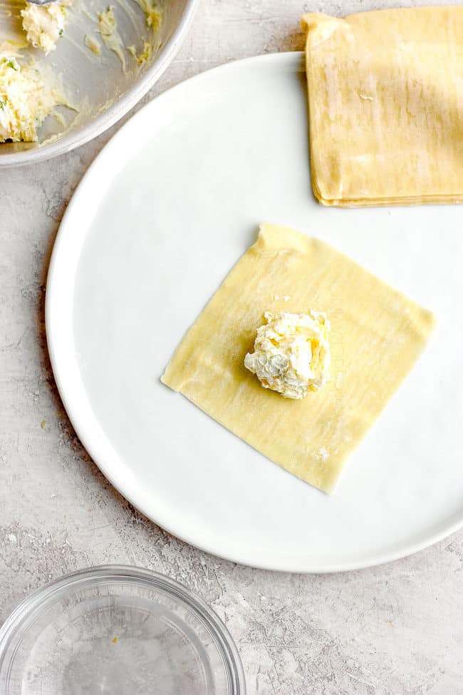 showing how to make cream cheese wontons by placing filling in a wonton wrapper