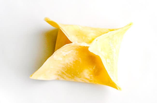 showing how to make cream cheese wontons by folding up all corners of wontons