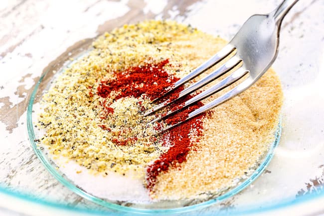showing how to make lemon pepper chicken by whisking lemon pepper, garlic, onion powder and paprika together in a glass bowl