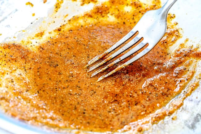 showing how to make lemon chicken marinade by whisking olive oil, lemon juice and spices together in a glass bowl