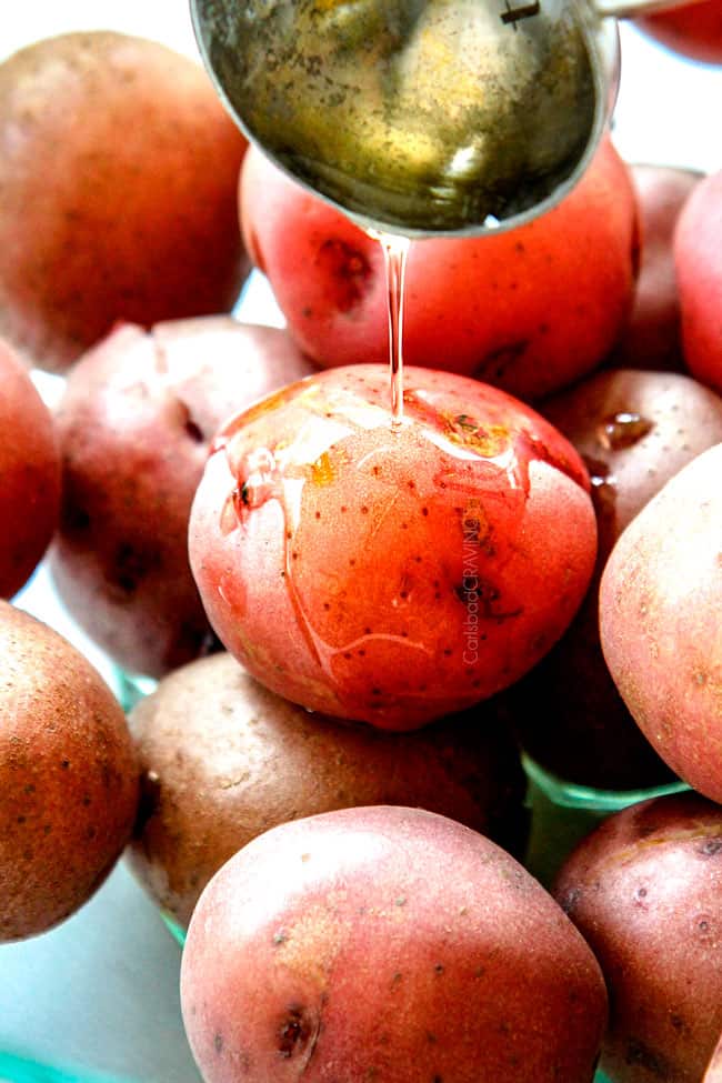 showing how to make smashed potatoes by adding oil to red potatoes in a glass bowl