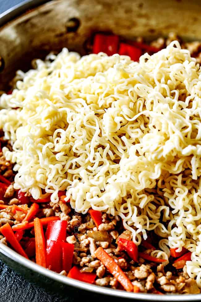 showing how to make ramen by adding ramen to chicken and vegetables in a skillet