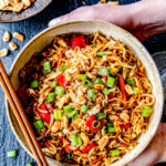 two hands holding a big bowl of spicy ramen with pork