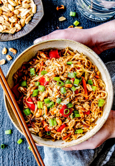 two hands holding a big bowl of spicy ramen with pork