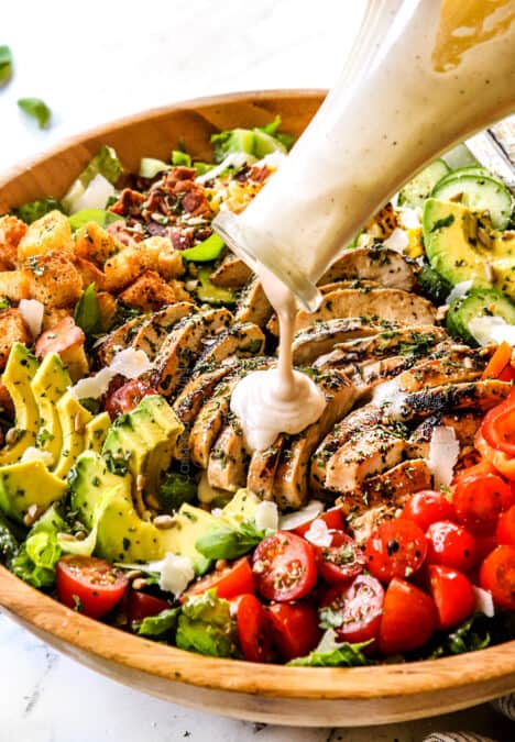 pouring Caesar dressing over a bowl of Chicken Caesar Salad