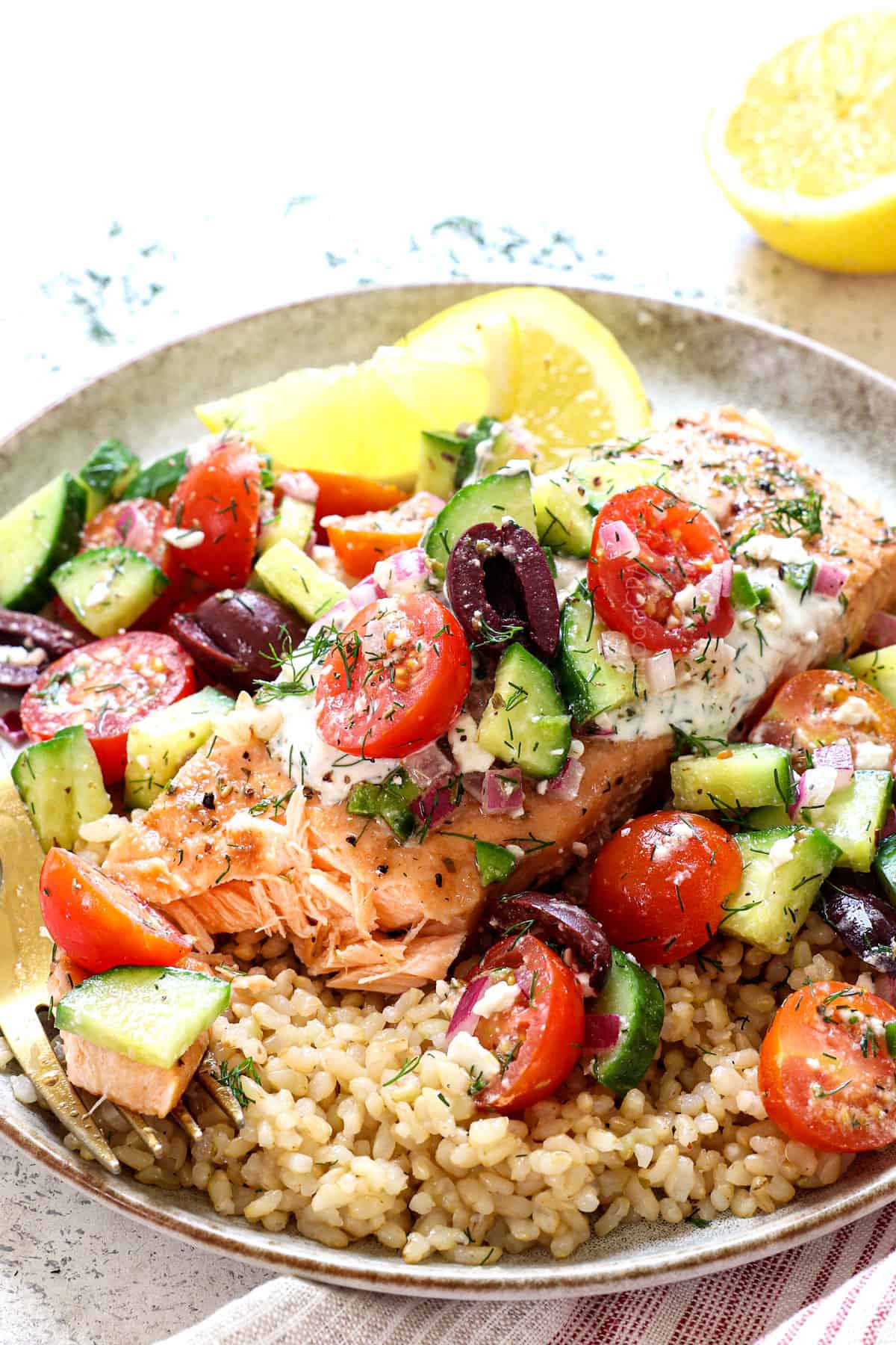 up close of serving baked salmon with dill sauce on a plate with a bite taken out showing how juicy the salmon is