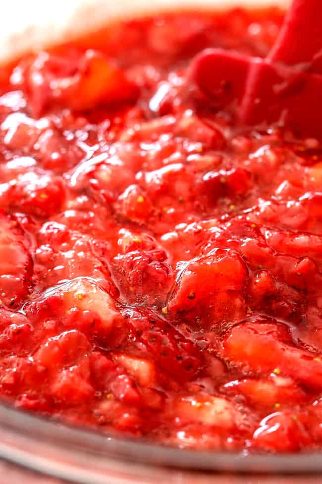 showing how to make strawberry shortcake cake by adding strawberry syrup to chopped strawberries