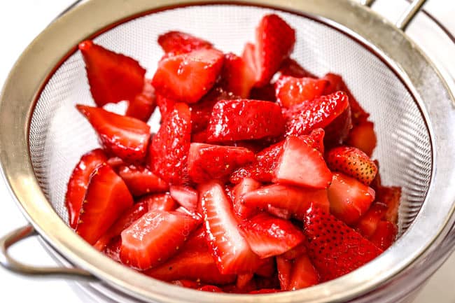 showing how to make strawberry shortcake cake strawberry filling by draining excess juices off of strawberries in a fine mesh sieve