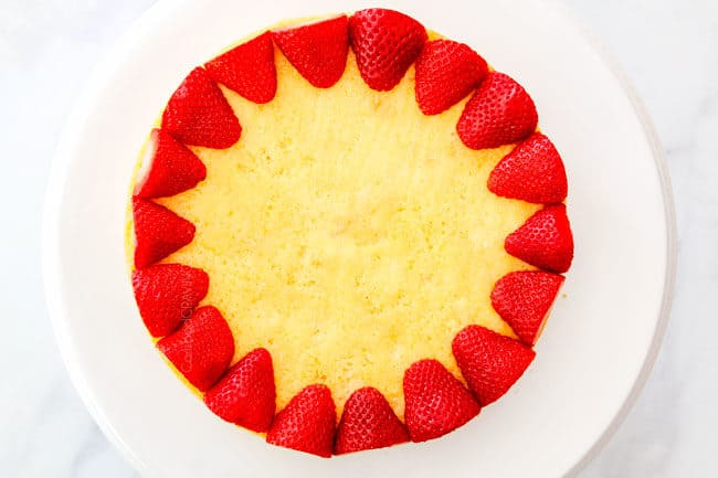 showing how to layer strawberry shortcake cake by lining halved strawberries all along the perimeter of a cake layer