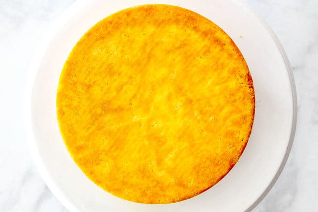 showing how to make strawberry shortcake cake by adding one cake layer to the center of a cake stand