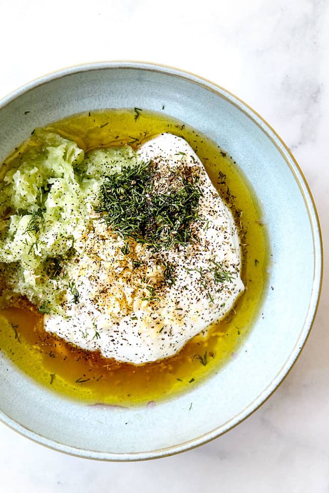 showing ingredients for Tzatziki in a bowl: Greek yogurt, garlic, cucumbers, dill, lemon juice, vinegar