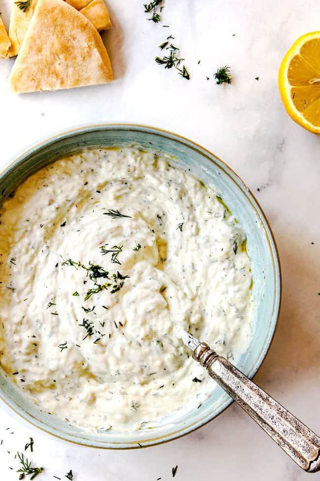 top view of Tzatziki sauce in a bowl with a spoon garnished by dill