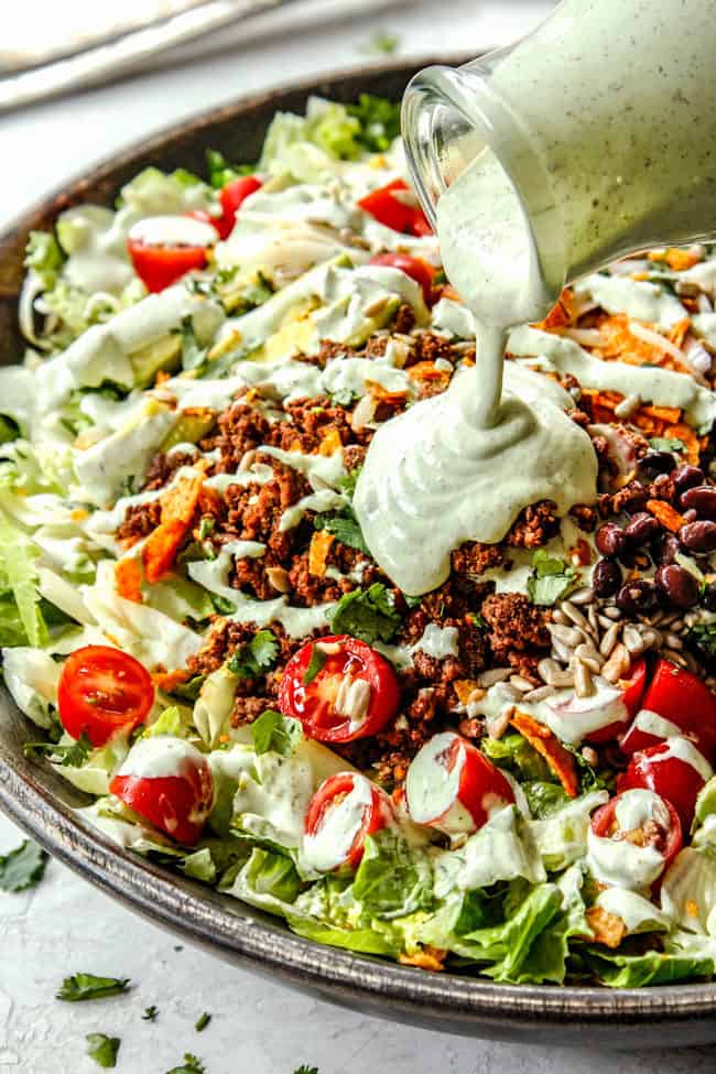 showing how to make taco salad by pouring taco salad dressing over salad
