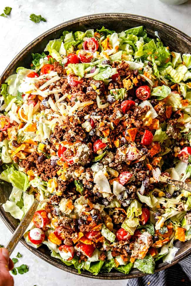 showing how to make taco salad by tossing all of the salad ingredients together