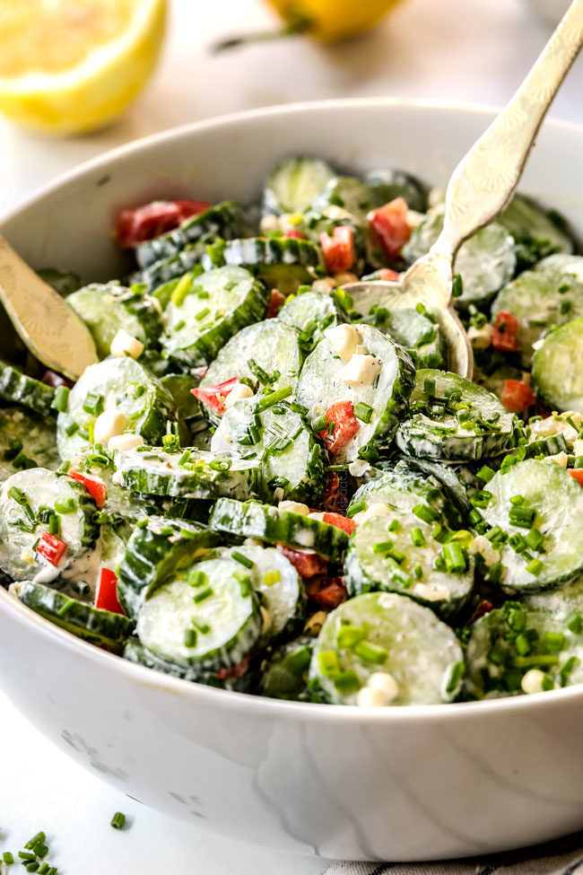 two golden serving spoons tossing cucumber salad with sour cream