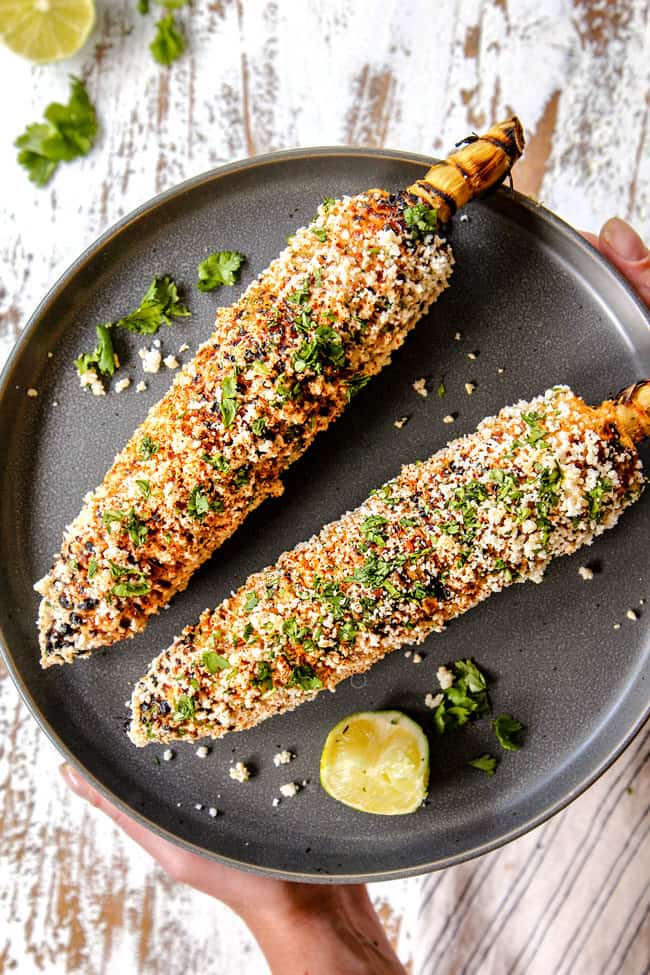 two hands holding a plate of elote recipe