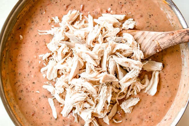 showing how to make cheesy chicken spaghetti by shredded chicken to chicken spaghetti sauce