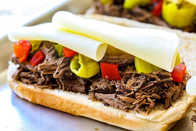 showing how to make crock pot Italian Beef sandwiches by layering the pepperoncini and roasted red bell peppers with provolone cheese