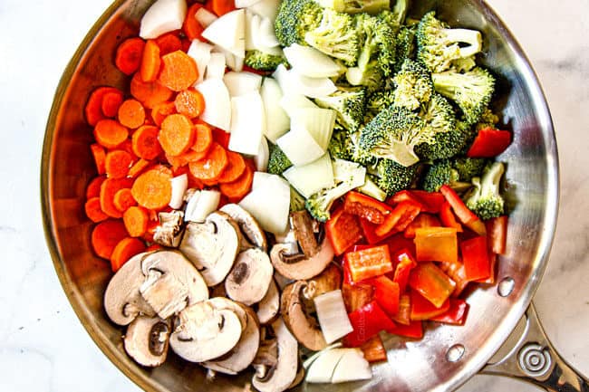 showing how to make easy chicken stir fry recipe by adding onions,s broccoli, carrots, bell peppers and mushrooms to skillet