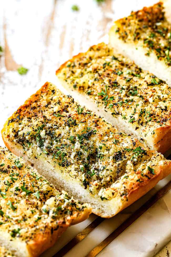 slices of the best garlic bread recipe on a marble cutting board garnished with parsley
