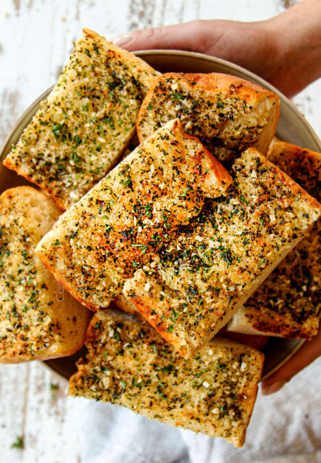 two hands holding a bowl of garlic bread in oven