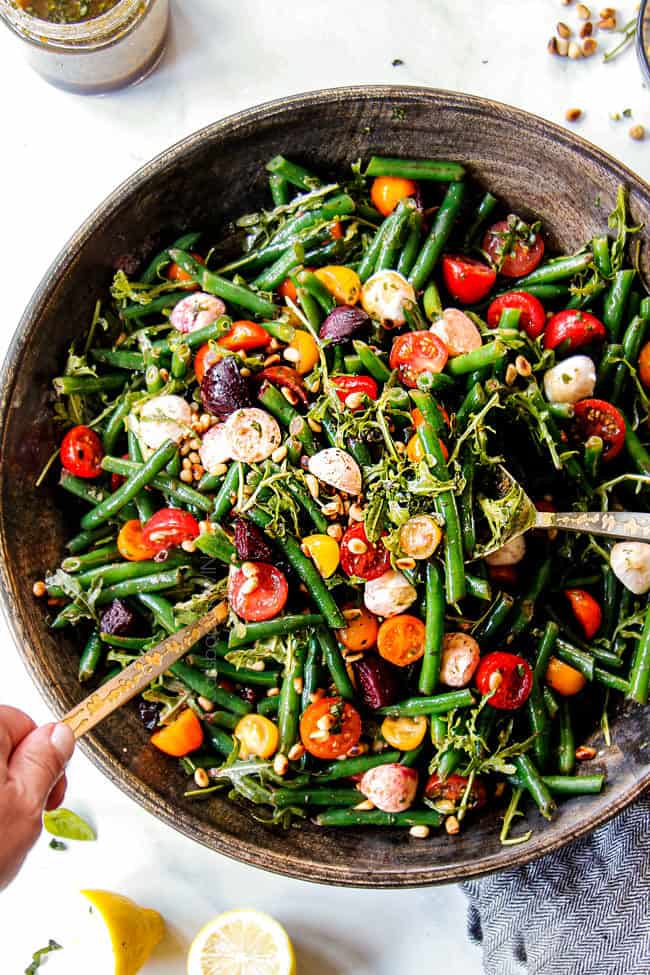 showing how to serve cold green bean salad by tossing salad with tongs
