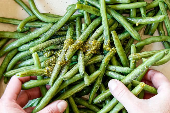 showing how to make pesto chicken by mixing green beans with pesto, olive oil, salt and pepper