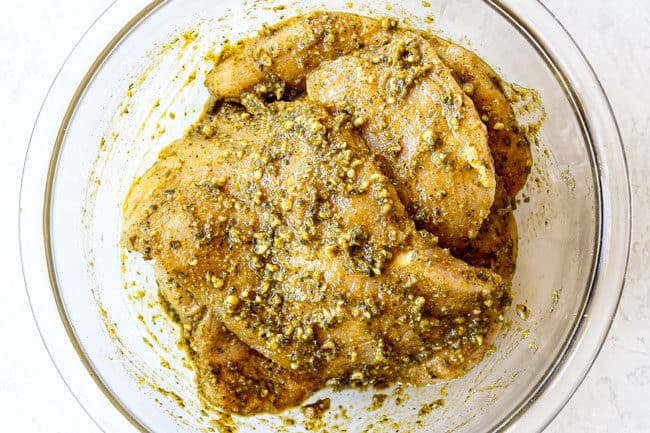 showing how to make pesto chicken by mixing chicken with pesto and seasonings