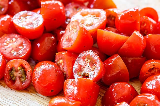 showing how to make pesto chicken recipe by tossing tomatoes with olive oil, salt and pepper