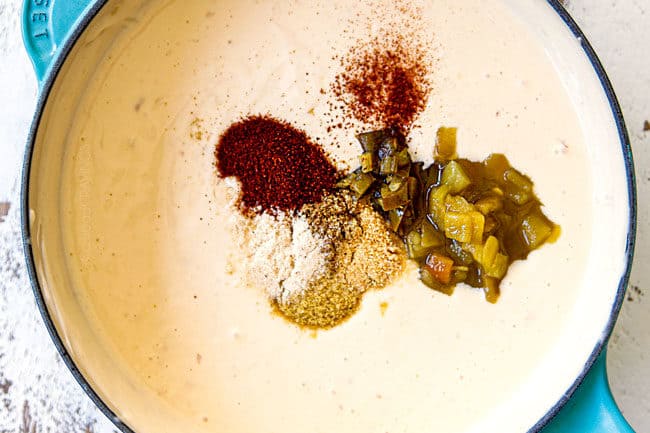 showing how to make queso blanco (white queso dip) by whisking in diced green chiles, jalapenos, chili powder, cumin, salt and pepper