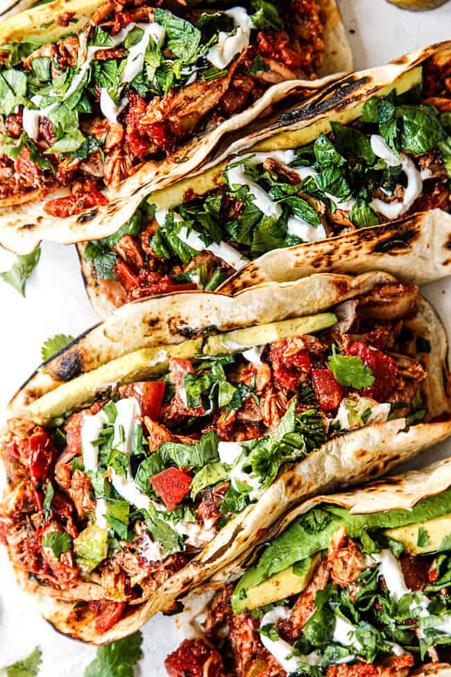 shredded chicken tacos recipe on a plate with cilantro, sour cream and avoados