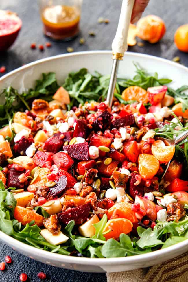 showing how to make beet goat cheese salad by tossing salad together with white salad tongs