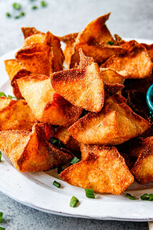 showing how to serve crab wontons by stacking on a plate with sweet and sour sauce