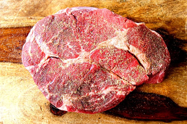 showing how to cook a roast in a crock pot by seasoning chuck roast with kosher salt and pepper