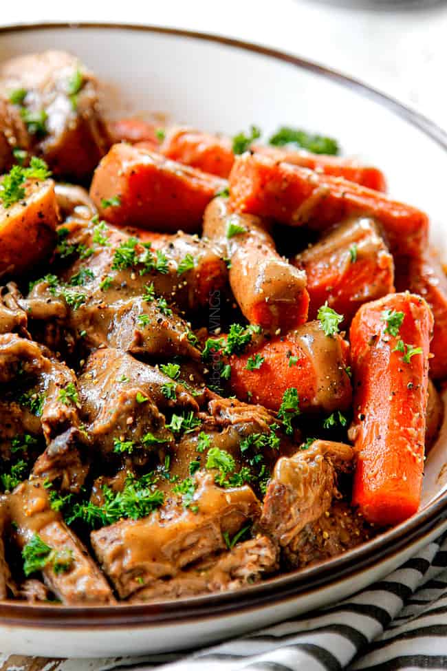 showing how to make slow cooker pot roast by adding chuck roast, potatoes and carrots to a bowl with gravy