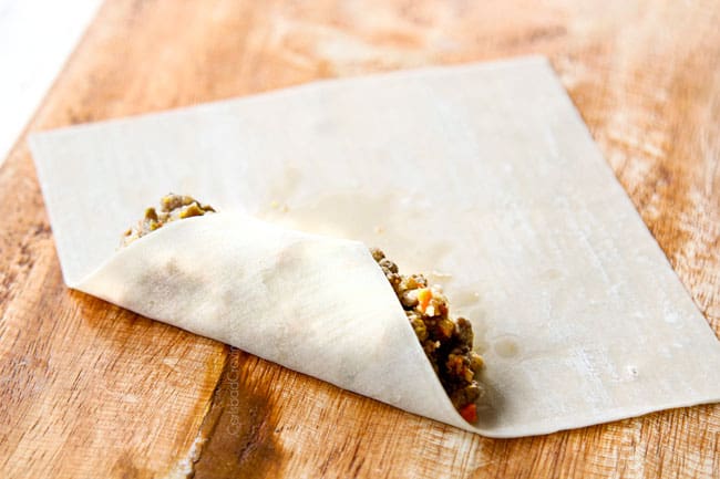 showing how to make homemade egg rolls by folding bottom corner over filling and pressing out air